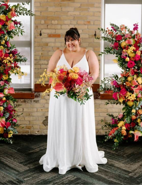Woman in a white wedding dress holding a bouquet of flowers in front of floral decorations.