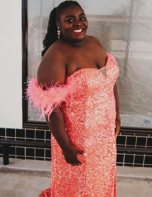 Woman in a pink sequin dress with feather sleeves standing against a wall.