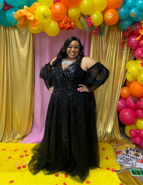 Woman in a black evening gown standing in front of colorful balloons and decorations.