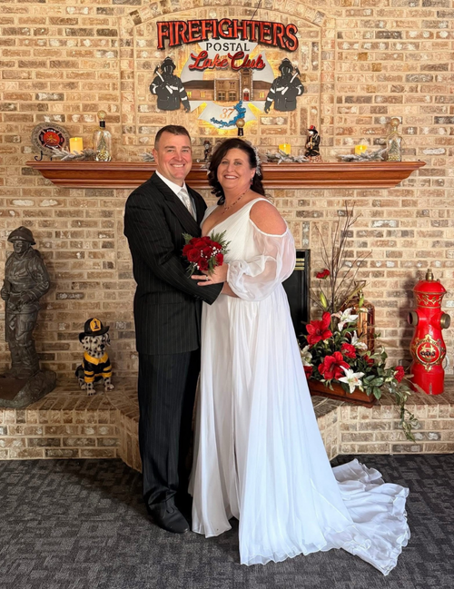 A bride and groom in formal wedding attire standing in front of a brick wall with decorative items.
