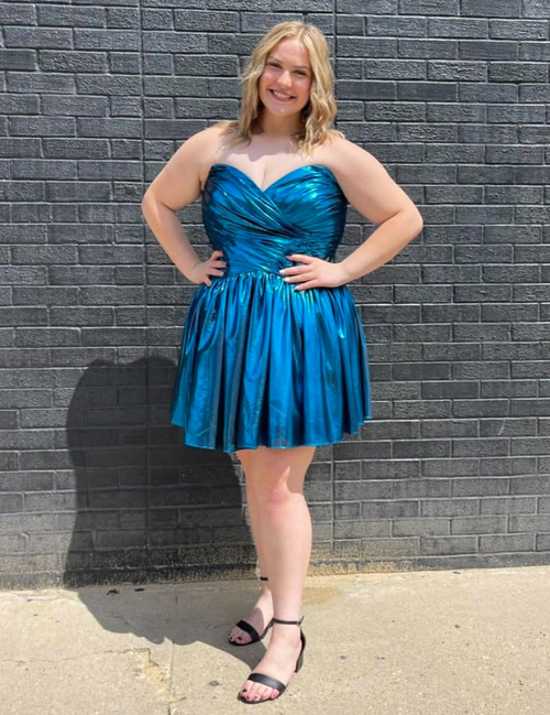 Woman in a blue dress standing against a gray brick wall.