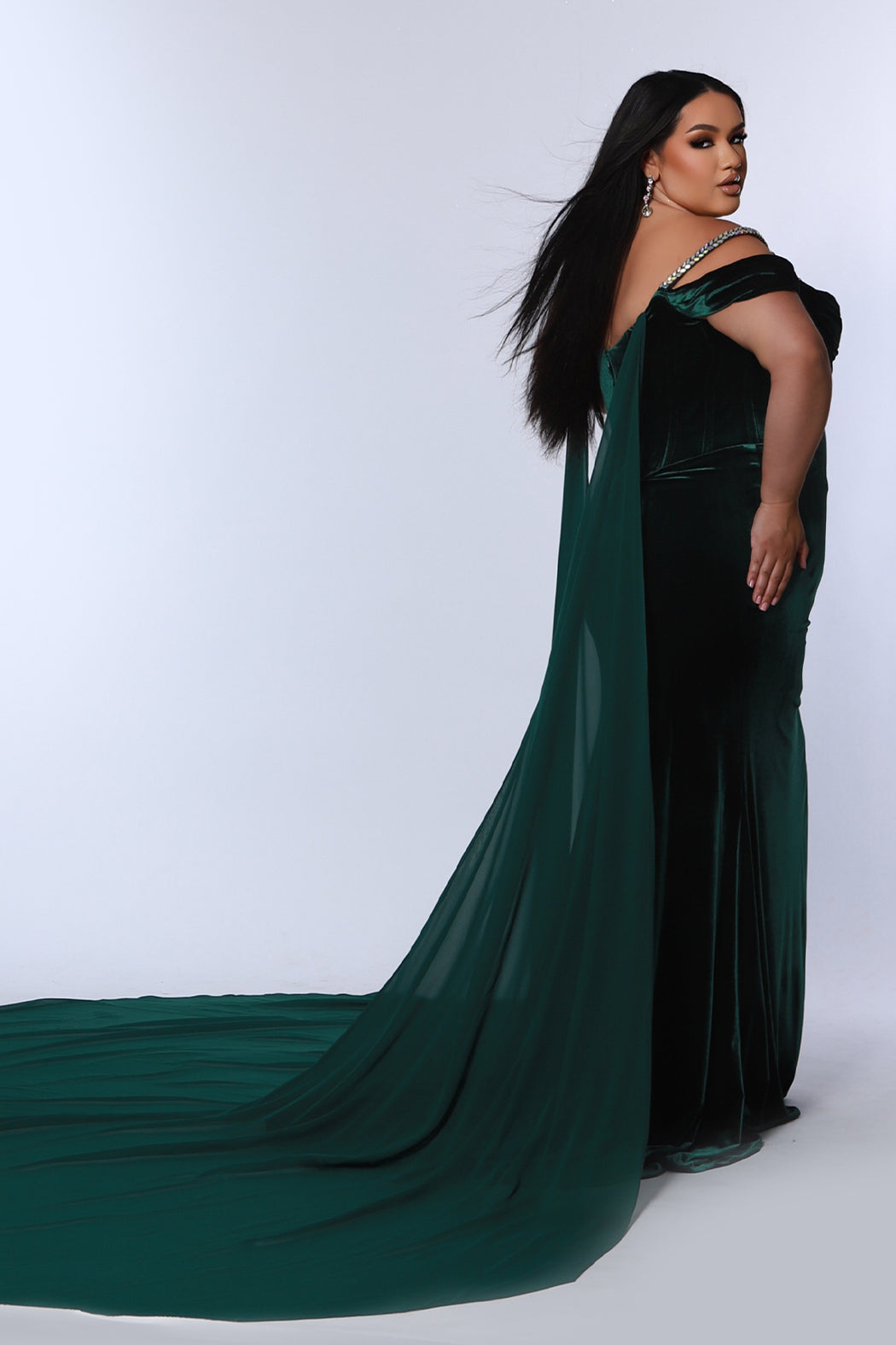 Johnathan Kayne for Sydney's Closet plus size pageant gown. Style JK2514 in stretch velvet with beaded bustier bodice and optional chiffon cape. Pleated drape on bodice with pleated detachable drape sleeves.  Exposed corset boning with basque waistline. Slim fitted skirt with ruching and high slit.  Availablie in forest green, onyx black or royal blue in plus sizes 10-24.