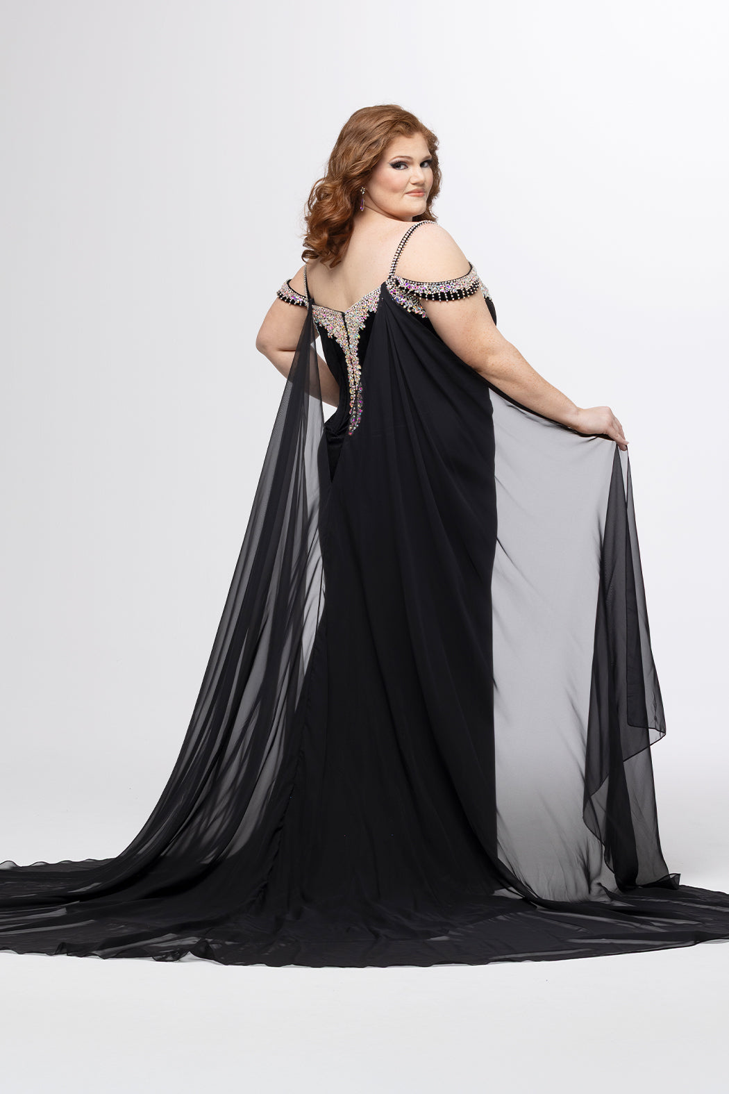 Johnathan Kayne for Sydney's Closet style JK2610.

Stretch velvet fitted plus size evening gown.  AB stoned v-neckline with stoned spaghetti straps. Off-the-shoulder stoned drapes straps, left leg slit and sweep train. Chiffon cape attached at back. Available in sizes 10-28 in black and royal blue. 
