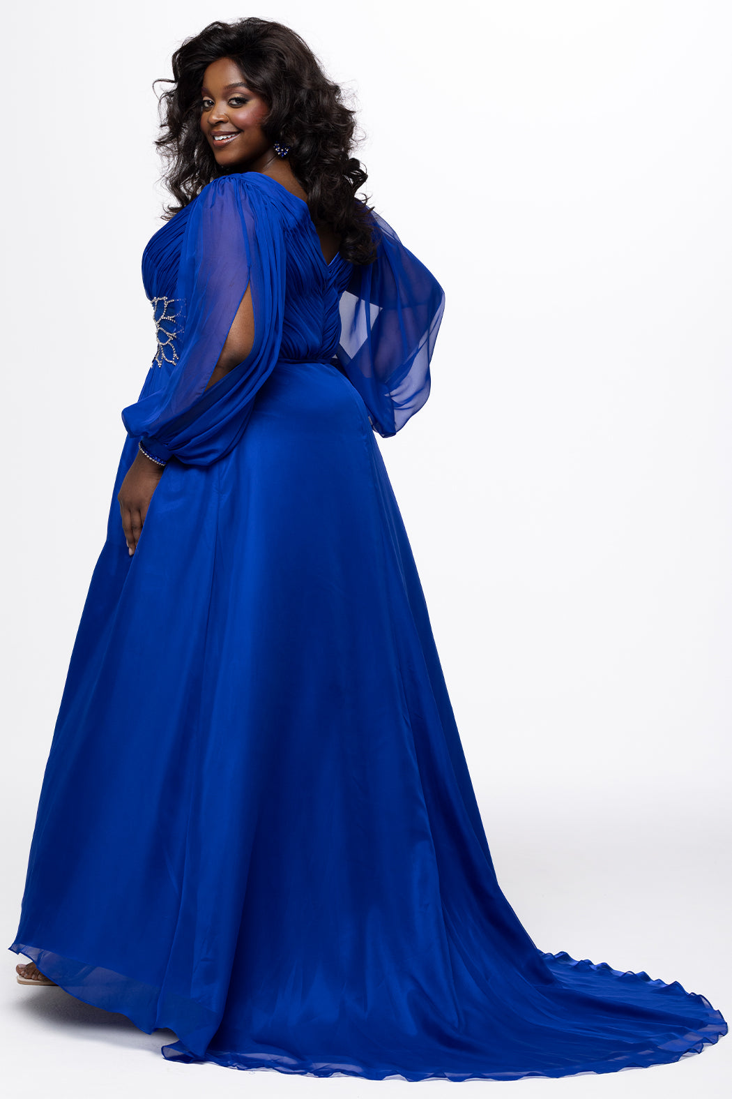 Johnathan Kayne for Sydney's Closet style JK2614. 

Plus size A-line chiffon gown with long bishop sleeves, beaded cuff and bicep slit. Bra-friendly straps, v-neckline and pleated bodice. Natural waistline with 4 inch beaded, rhinestone and sequin embellished waistband. Pockets, left leg slit with zipper, v-back and center back zipper. Available in sizes 10-32 in black, blue and red. 