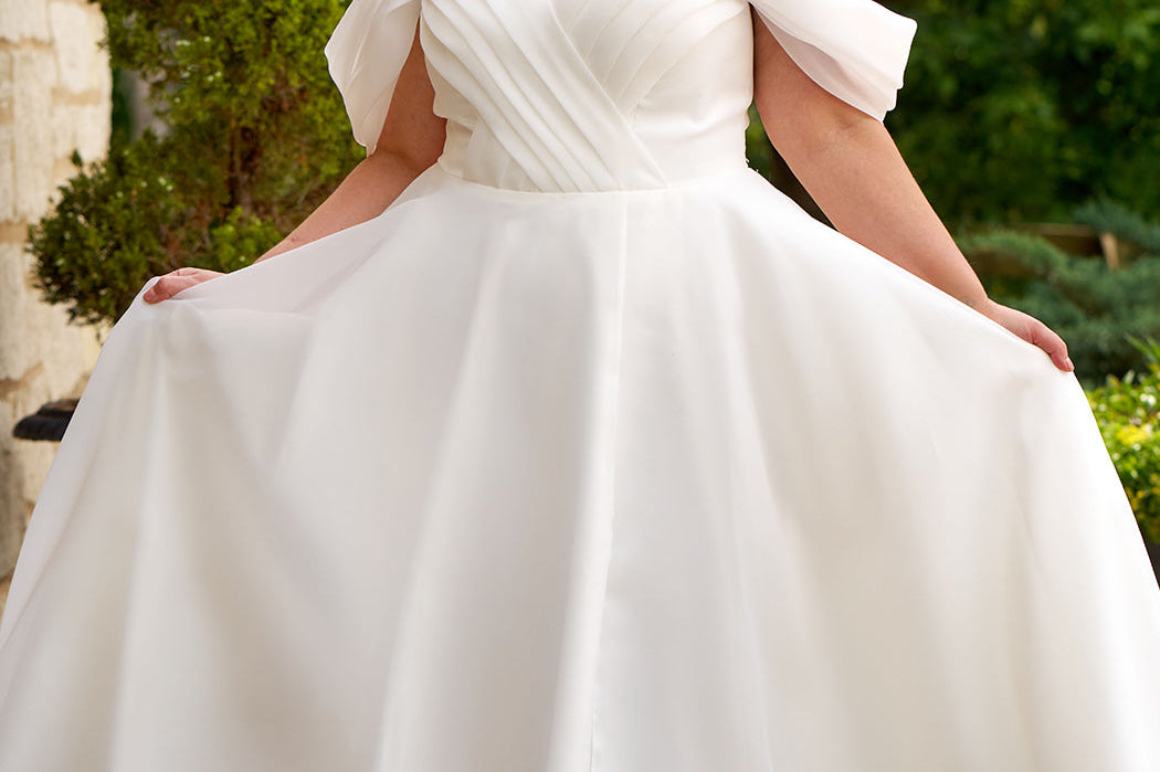 Michelle Bridal MB2506 plus size wedding dress by Sydney's Closet. Off-the-shoulder pleated straps, organza ballgown with slit and long train available in black, ivory or mauve pink