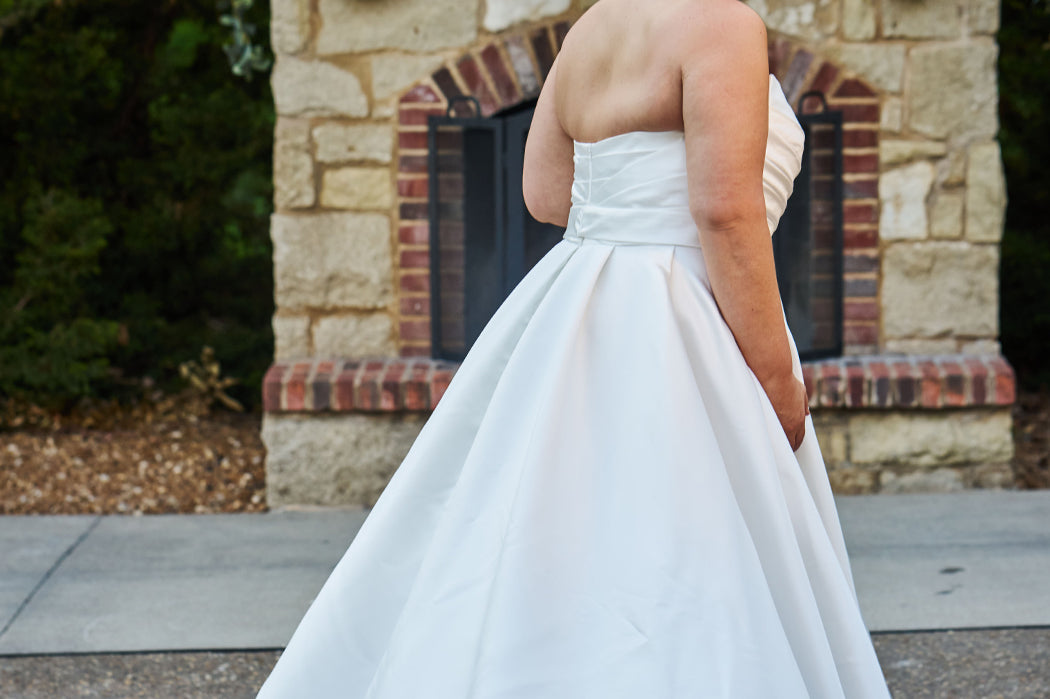 Strapless satin plus size wedding gown with pleated bodice and detachable belt included. A-line skirt with box pleats, pockets and long train. Michelle Bridal style MB2523 is available in ivory or black. 