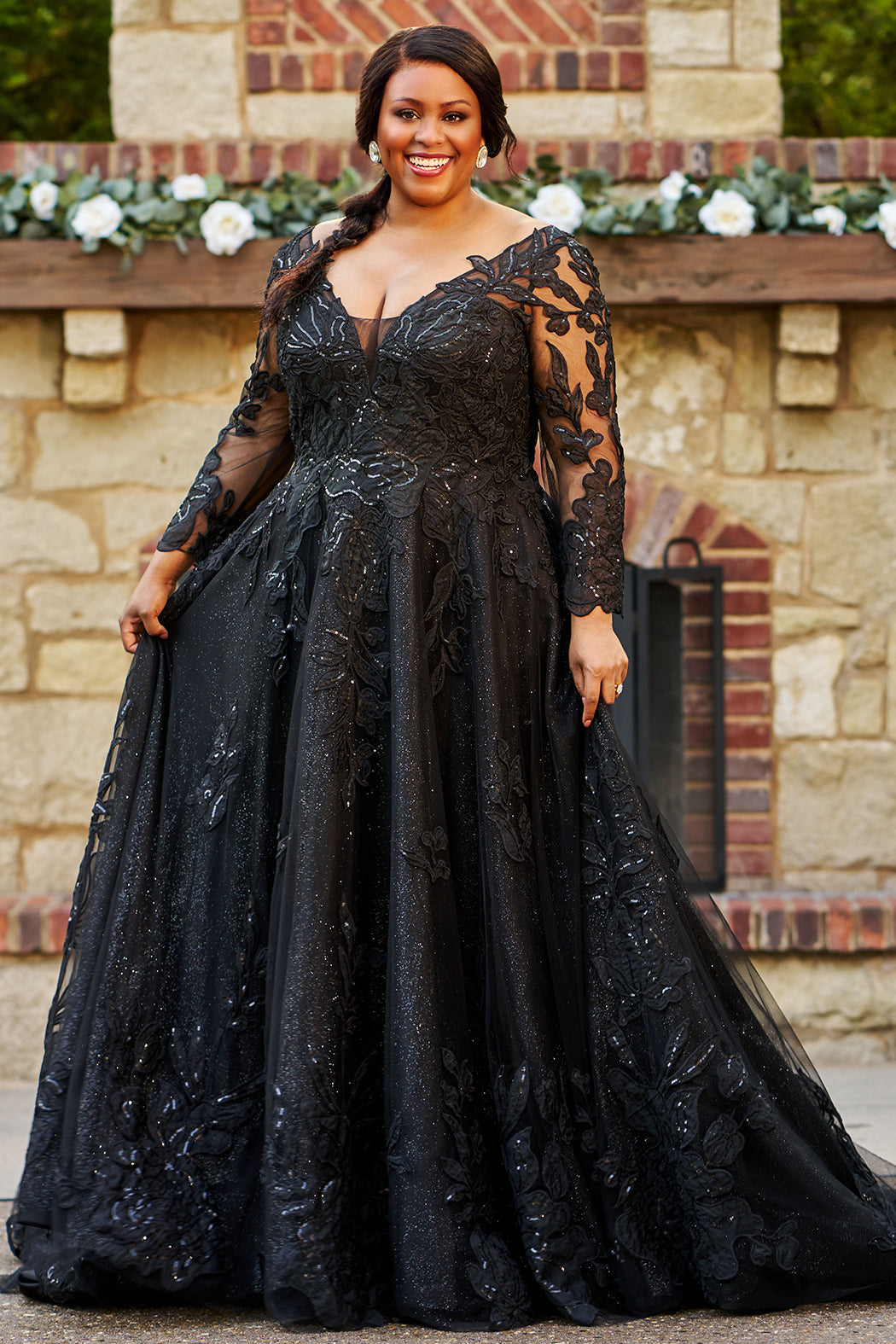 MB2604 by Michelle Bridal

Available in Black, Ivory, Black on Ivory, Ivory on Black, Ivory on Champagne and Black on Champagne. 

Plus-size model wearing a black A-line wedding gown with sheer long sleeves, a deep V-neckline, and intricate lace appliqué with subtle shimmer throughout the full skirt, photographed outdoors in front of a stone backdrop.