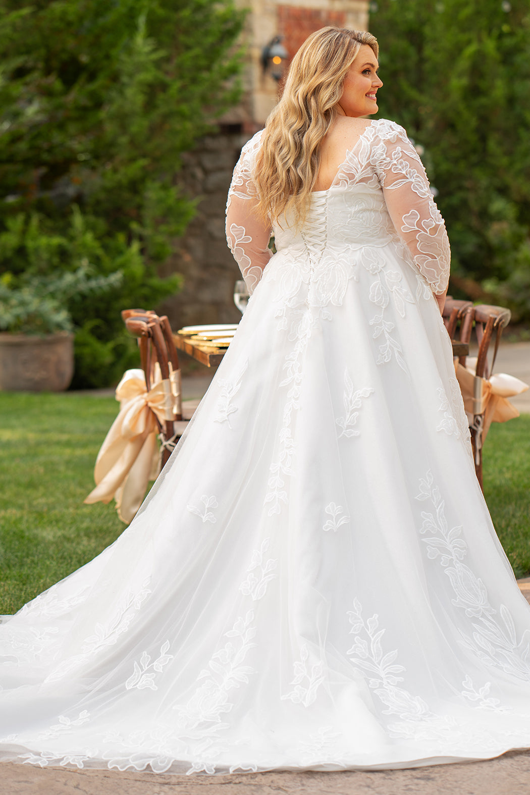 MB2604 by Michelle Bridal

Available in Black, Ivory, Black on Ivory, Ivory on Black, Ivory on Champagne and Black on Champagne. 

Plus-size model wearing an ivory A-line wedding gown with sheer long sleeves, a deep V-neckline, and intricate lace appliqué with subtle shimmer throughout the full skirt, photographed outdoors in front of a stone backdrop.