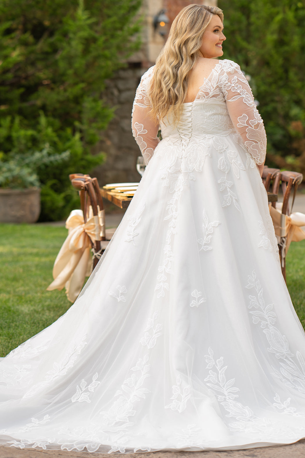 MB2604 by Michelle Bridal

Available in Black, Ivory, Black on Ivory, Ivory on Black, Ivory on Champagne and Black on Champagne. 

Plus-size model wearing an ivory A-line wedding gown with sheer long sleeves, a deep V-neckline, and intricate lace appliqué with subtle shimmer throughout the full skirt, photographed outdoors in front of a stone backdrop.