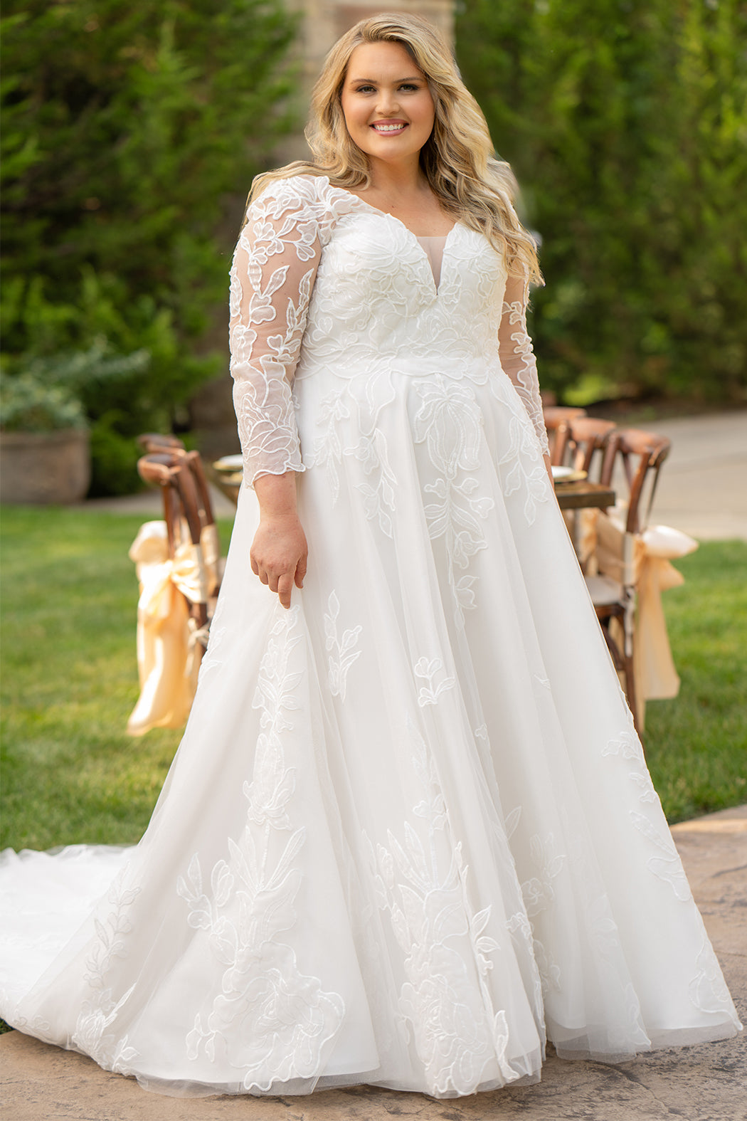 MB2604 by Michelle Bridal

Available in Black, Ivory, Black on Ivory, Ivory on Black, Ivory on Champagne and Black on Champagne. 

Plus-size model wearing an ivory A-line wedding gown with sheer long sleeves, a deep V-neckline, and intricate lace appliqué with subtle shimmer throughout the full skirt, photographed outdoors in front of a stone backdrop.