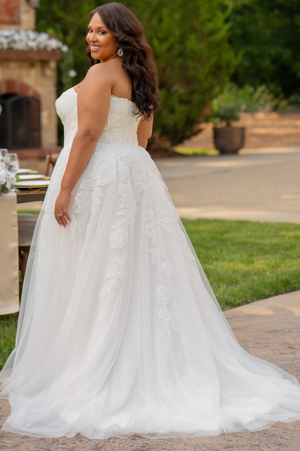 Michelle Bridal MB2605. Strapless A-line gown with bodice drape detail, exposed boning, basque waistline and soft tulle A-Line skirt. Large embroidered organza appliques. Center back zipper. 