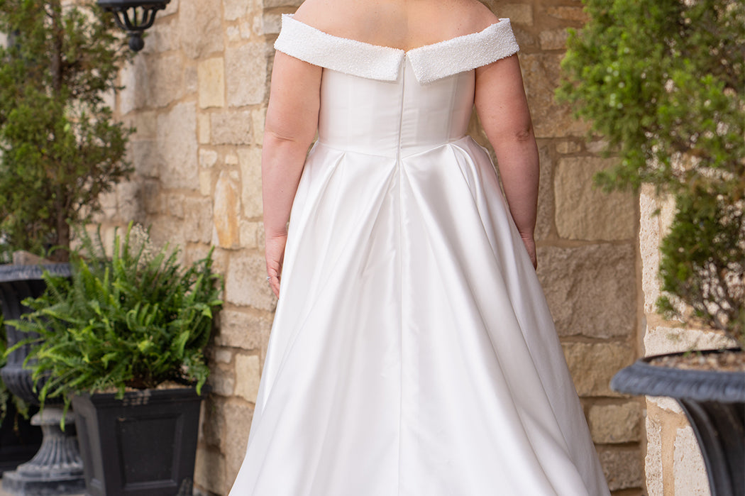 Michelle Bridal MB2610 shown in ivory. Off-the-shoulder satin A-line gown, bodice cuff covered in pearls and clear beads. Natural waistline, box pleats on skirt and center back zipper. Long satin train. 