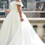 Michelle Bridal MB2610 shown in ivory. Off-the-shoulder satin A-line gown, bodice cuff covered in pearls and clear beads. Natural waistline, box pleats on skirt and center back zipper. Long satin train. 