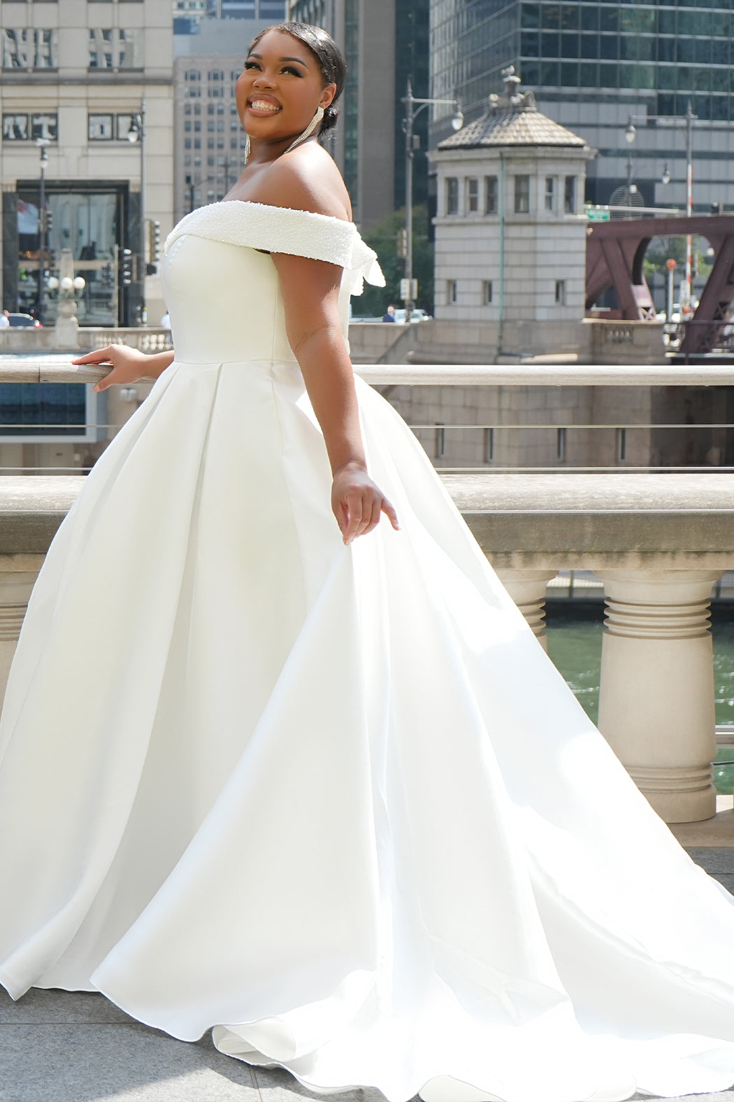 Michelle Bridal MB2610 shown in ivory. Off-the-shoulder satin A-line gown, bodice cuff covered in pearls and clear beads. Natural waistline, box pleats on skirt and center back zipper. Long satin train. 