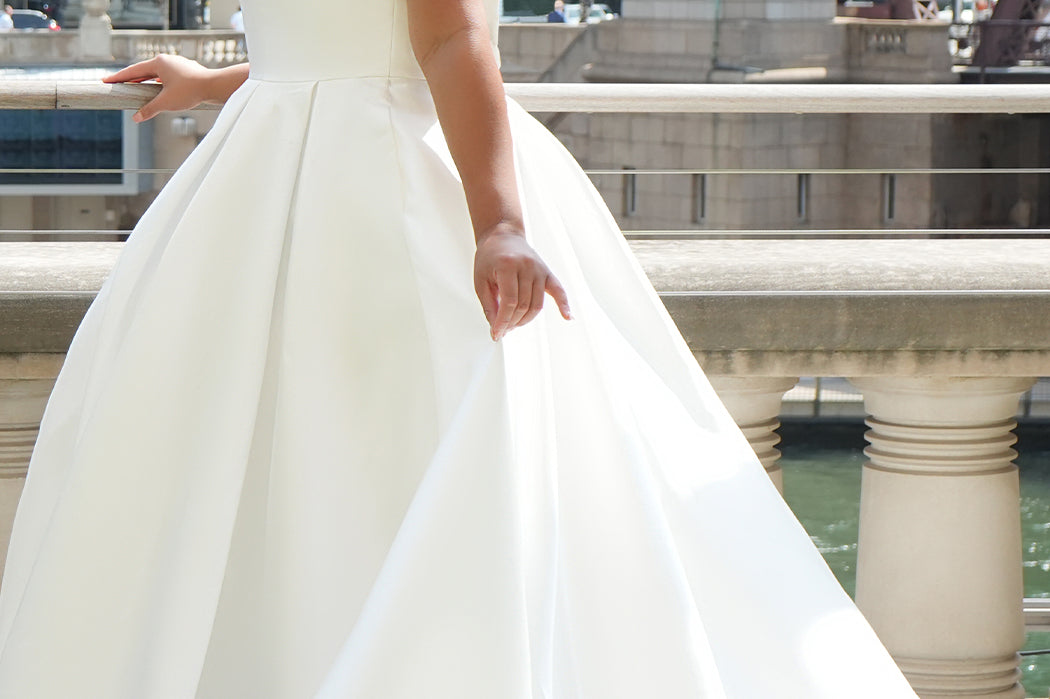 Michelle Bridal MB2610 shown in ivory. Off-the-shoulder satin A-line gown, bodice cuff covered in pearls and clear beads. Natural waistline, box pleats on skirt and center back zipper. Long satin train. 