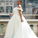 Michelle Bridal MB2610 shown in ivory. Off-the-shoulder satin A-line gown, bodice cuff covered in pearls and clear beads. Natural waistline, box pleats on skirt and center back zipper. Long satin train. 