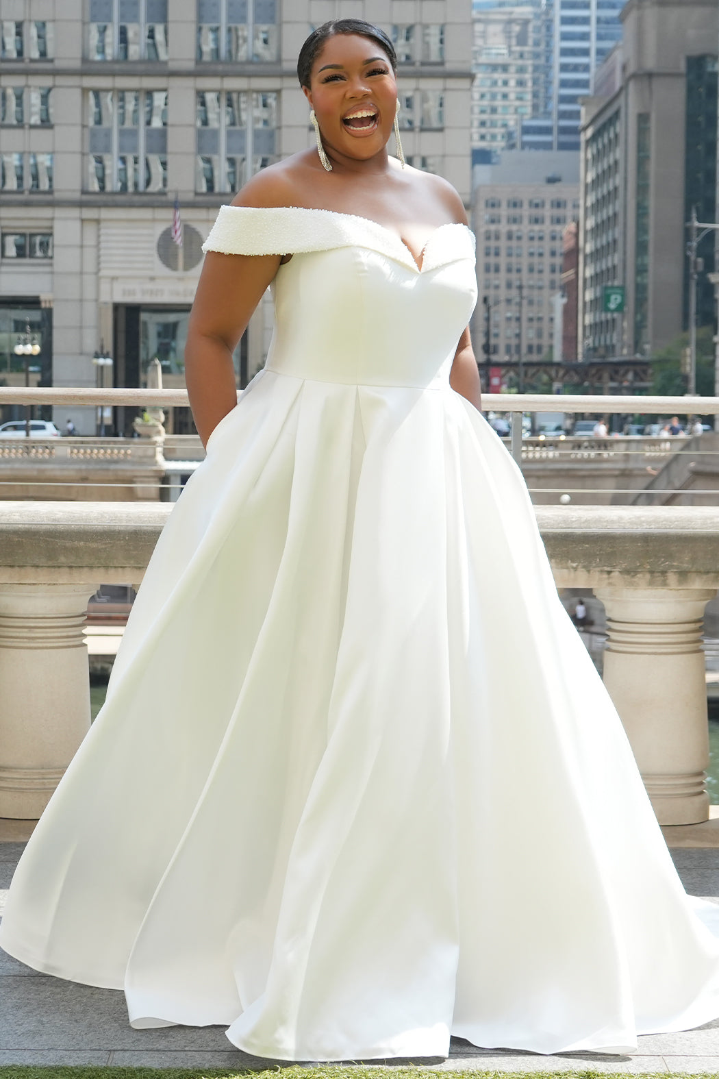 Michelle Bridal MB2610 shown in ivory. Off-the-shoulder satin A-line gown, bodice cuff covered in pearls and clear beads. Natural waistline, box pleats on skirt and center back zipper. Long satin train. 
