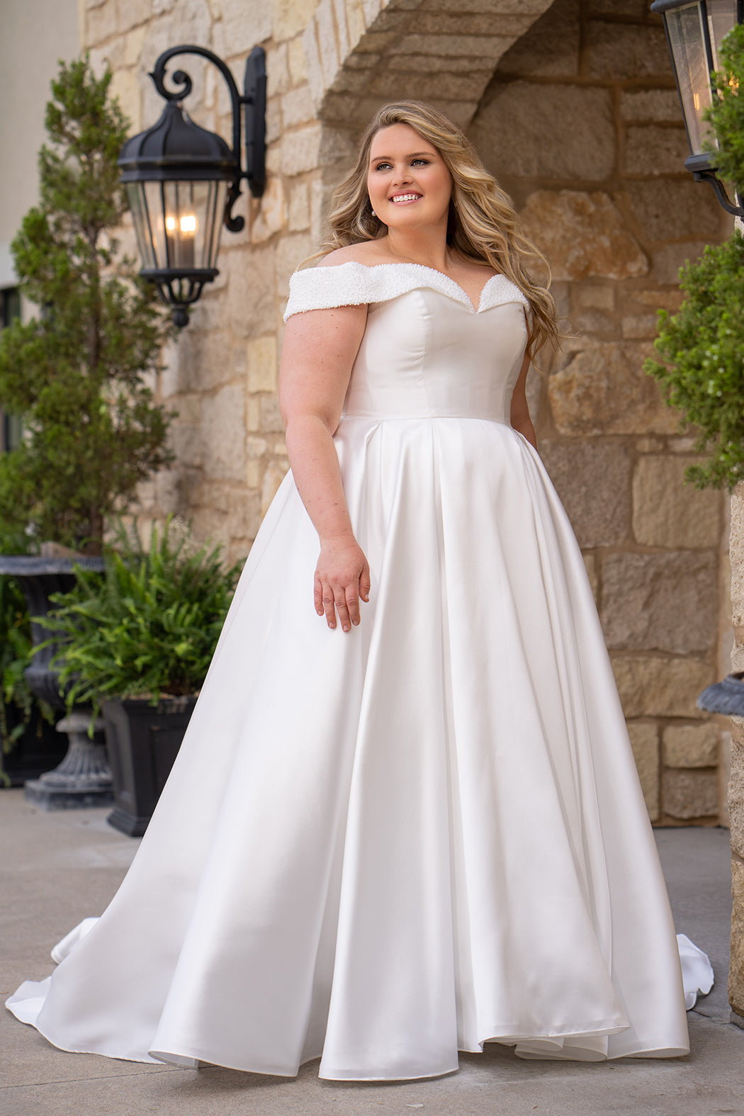 Michelle Bridal MB2610 shown in ivory. Off-the-shoulder satin A-line gown, bodice cuff covered in pearls and clear beads. Natural waistline, box pleats on skirt and center back zipper. Long satin train. 