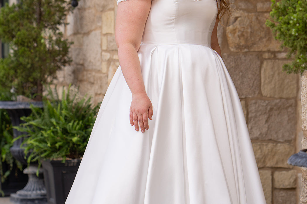 Michelle Bridal MB2610 shown in ivory. Off-the-shoulder satin A-line gown, bodice cuff covered in pearls and clear beads. Natural waistline, box pleats on skirt and center back zipper. Long satin train. 