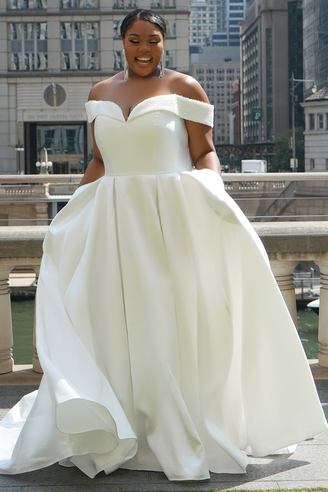 Michelle Bridal MB2610 shown in ivory. Off-the-shoulder satin A-line gown, bodice cuff covered in pearls and clear beads. Natural waistline, box pleats on skirt and center back zipper. Long satin train. 