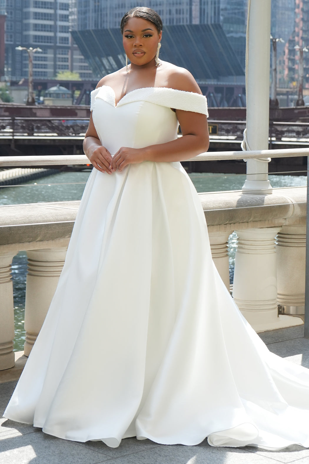 Michelle Bridal MB2610 shown in ivory. Off-the-shoulder satin A-line gown, bodice cuff covered in pearls and clear beads. Natural waistline, box pleats on skirt and center back zipper. Long satin train. 