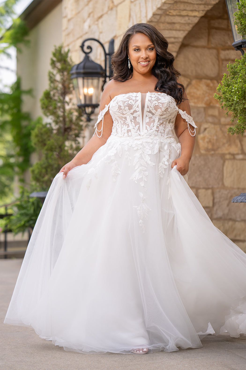 Michelle Bridal MB2611 shown in Ivory/Nude. 
Strapless bodice with deep v-neckline, exposed boning and optional drape straps with beaded detail. Soft bridal tulle A-line skirt with floral appliques, center back zipper. 