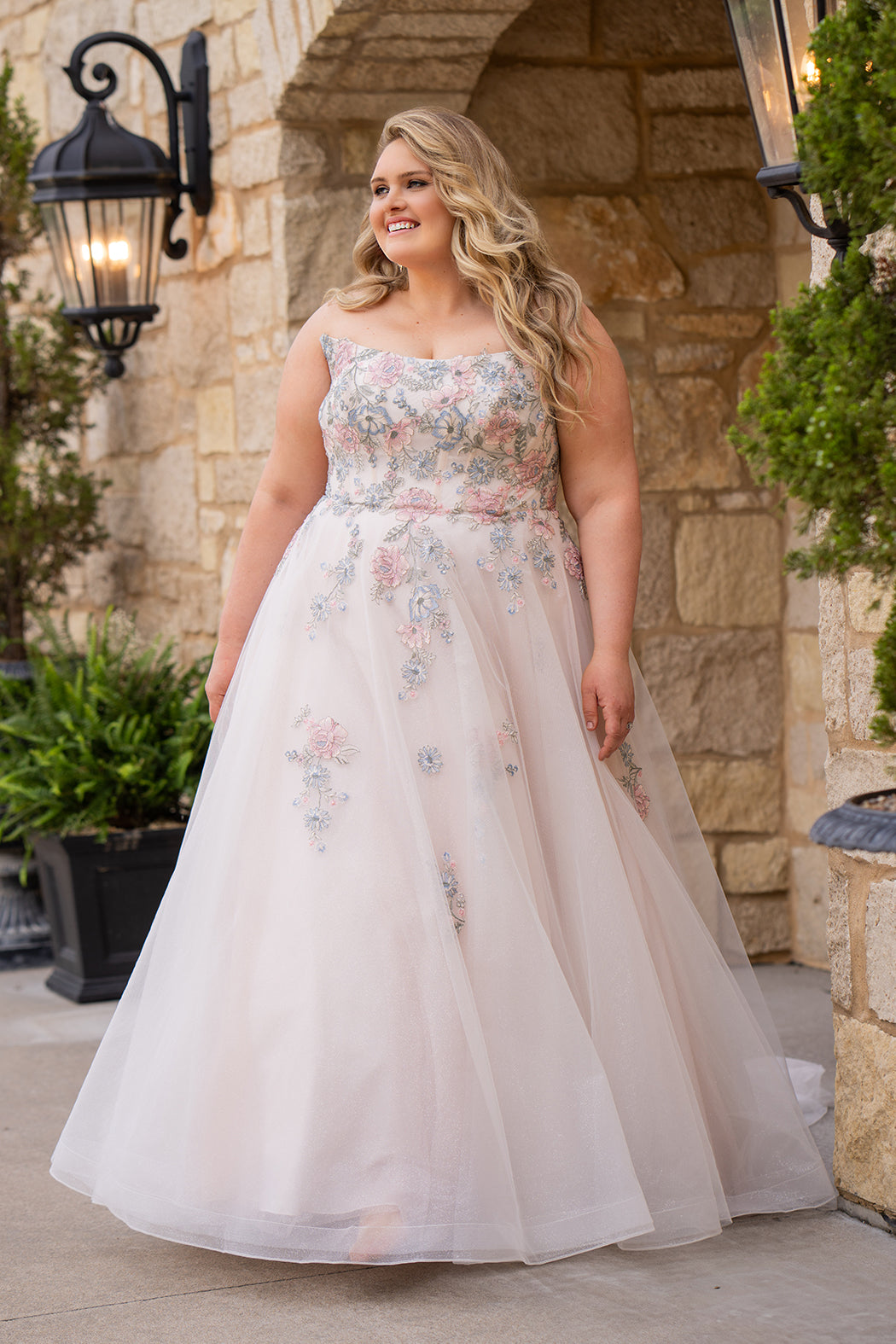Michelle Bridal MB2614 in Floral. 
Strapless scoop bodice, cat eye detail, pink and blue floral appliques. Natural waistline, A-line skirt, tulle and sparkle tulle layers over lightweight soft pink satin lining. Horse hair hem, scoop back and center back zipper. 