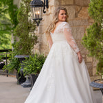 Michelle Bridal MB2615 shown in Ivory. 
Long sleeves covered in large organza appliques, v-neckline, 3 inch waistband. A-line skirt, Soft bridal tulle, large organa appliques, lightweight satin lining. V-Back, Long train and center back zipper. 