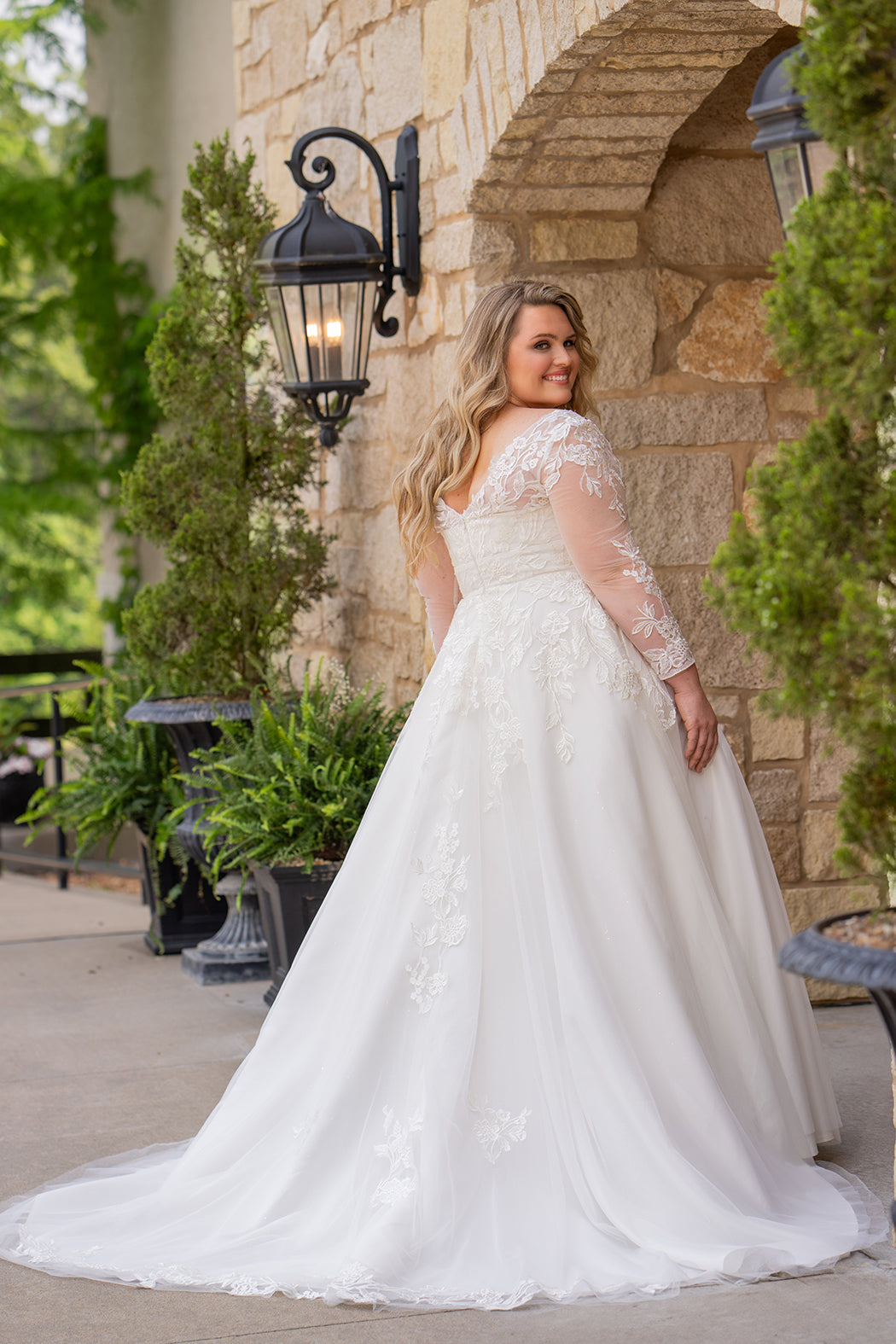 Michelle Bridal MB2615 shown in Ivory. 
Long sleeves covered in large organza appliques, v-neckline, 3 inch waistband. A-line skirt, Soft bridal tulle, large organa appliques, lightweight satin lining. V-Back, Long train and center back zipper. 