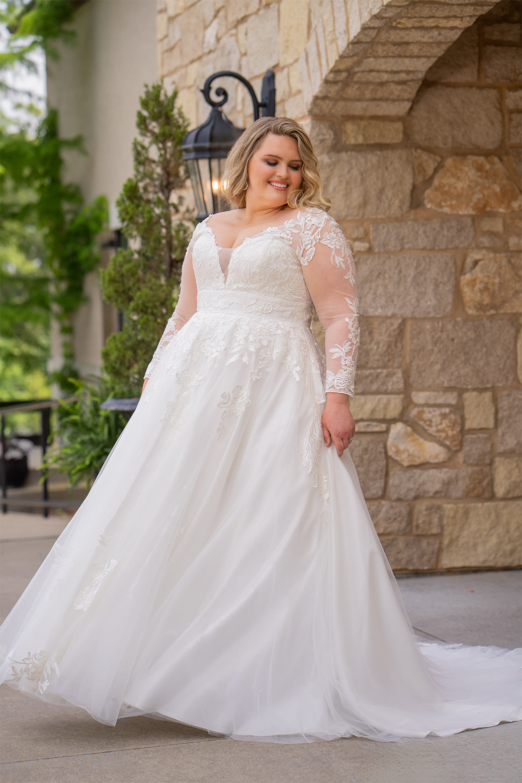 Michelle Bridal MB2615 shown in Ivory. 
Long sleeves covered in large organza appliques, v-neckline, 3 inch waistband. A-line skirt, Soft bridal tulle, large organa appliques, lightweight satin lining. V-Back, Long train and center back zipper. 