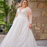 Michelle Bridal MB2615 shown in Ivory. 
Long sleeves covered in large organza appliques, v-neckline, 3 inch waistband. A-line skirt, Soft bridal tulle, large organa appliques, lightweight satin lining. V-Back, Long train and center back zipper. 