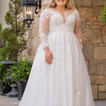 Michelle Bridal MB2615 shown in Ivory. 
Long sleeves covered in large organza appliques, v-neckline, 3 inch waistband. A-line skirt, Soft bridal tulle, large organa appliques, lightweight satin lining. V-Back, Long train and center back zipper. 