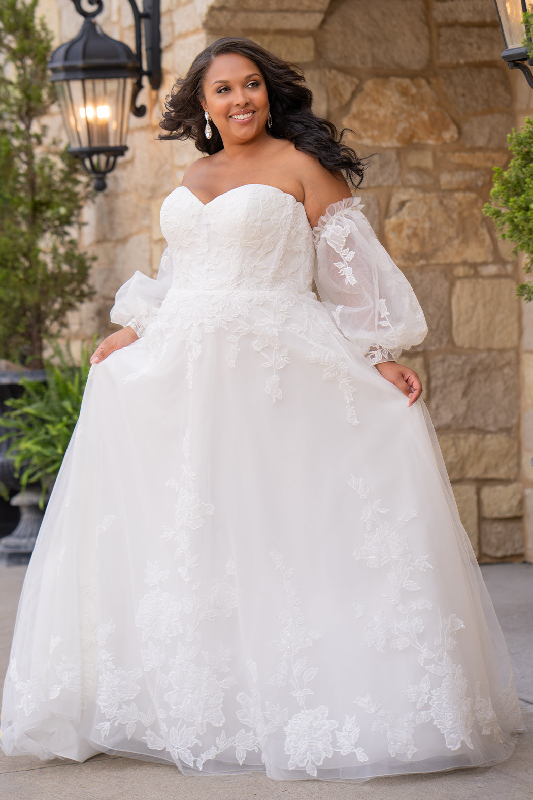 Michelle Bridal MB2618 shown in Ivory. 

Strapless sweetheart ballgown. Soft bridal tulle, floral lace appliques, lightweight satin lining. Natural waistline, A-Line skirt. Bicep optional puff sleeves. Straight across back, center back zipper, train and covered buttons. 
