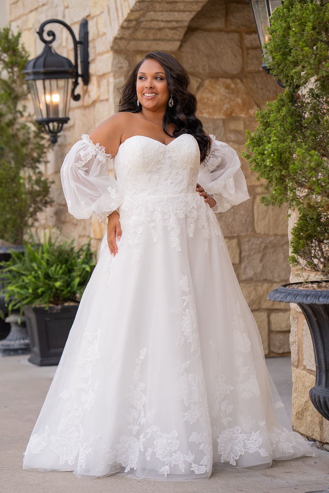 Michelle Bridal MB2618 shown in Ivory. 

Strapless sweetheart ballgown. Soft bridal tulle, floral lace appliques, lightweight satin lining. Natural waistline, A-Line skirt. Bicep optional puff sleeves. Straight across back, center back zipper, train and covered buttons. 