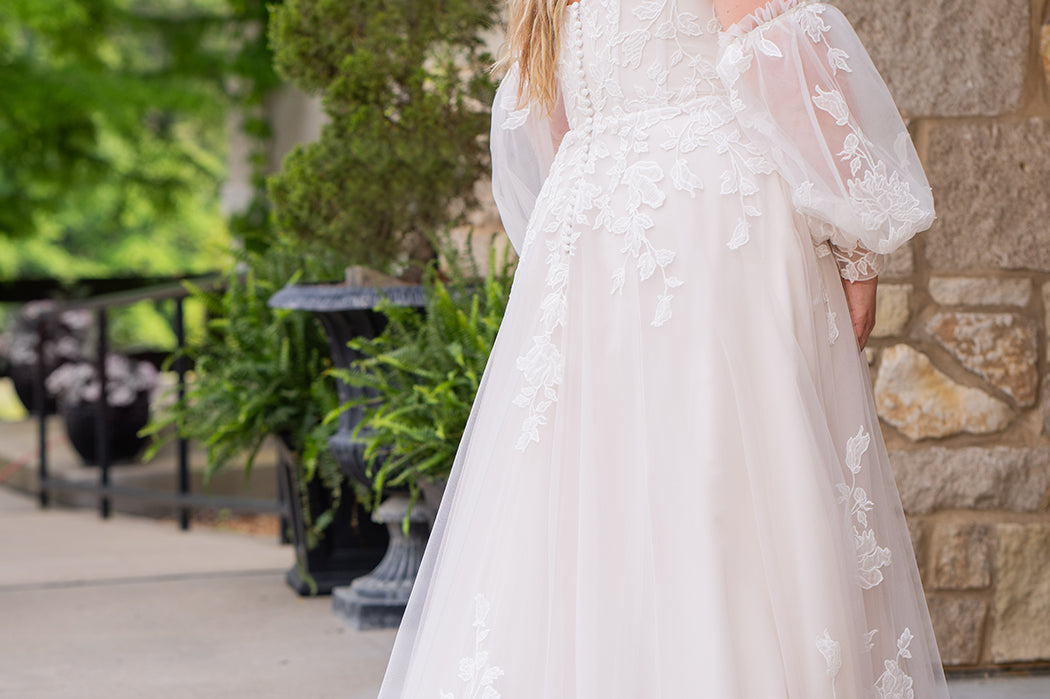 Michelle Bridal MB2618 shown in Sand. 

Strapless sweetheart ballgown. Soft bridal tulle, floral lace appliques, lightweight satin lining. Natural waistline, A-Line skirt. Bicep optional puff sleeves. Straight across back, center back zipper, train and covered buttons. 
