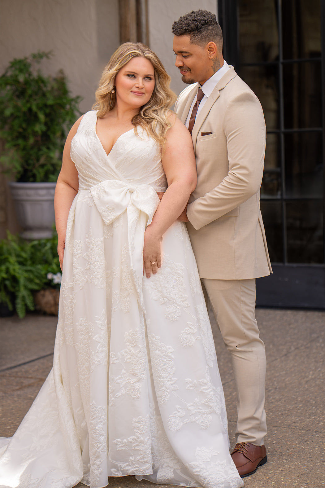 Michelle Bridal MB2625 shown in Ivory. 

Organza brocade A-line silhouette, Pleated faux surplice bodice for elegant shaping, Bra-friendly straps and sleeveless, detachable belt with oversized bow for two looks in one, Box-pleated A-line skirt with front slit for movement, Chapel-length train for timeless finish, Invisible center back zipper.