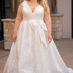 Michelle Bridal MB2625 shown in Ivory. 

Organza brocade A-line silhouette, Pleated faux surplice bodice for elegant shaping, Bra-friendly straps and sleeveless, detachable belt with oversized bow for two looks in one, Box-pleated A-line skirt with front slit for movement, Chapel-length train for timeless finish, Invisible center back zipper.