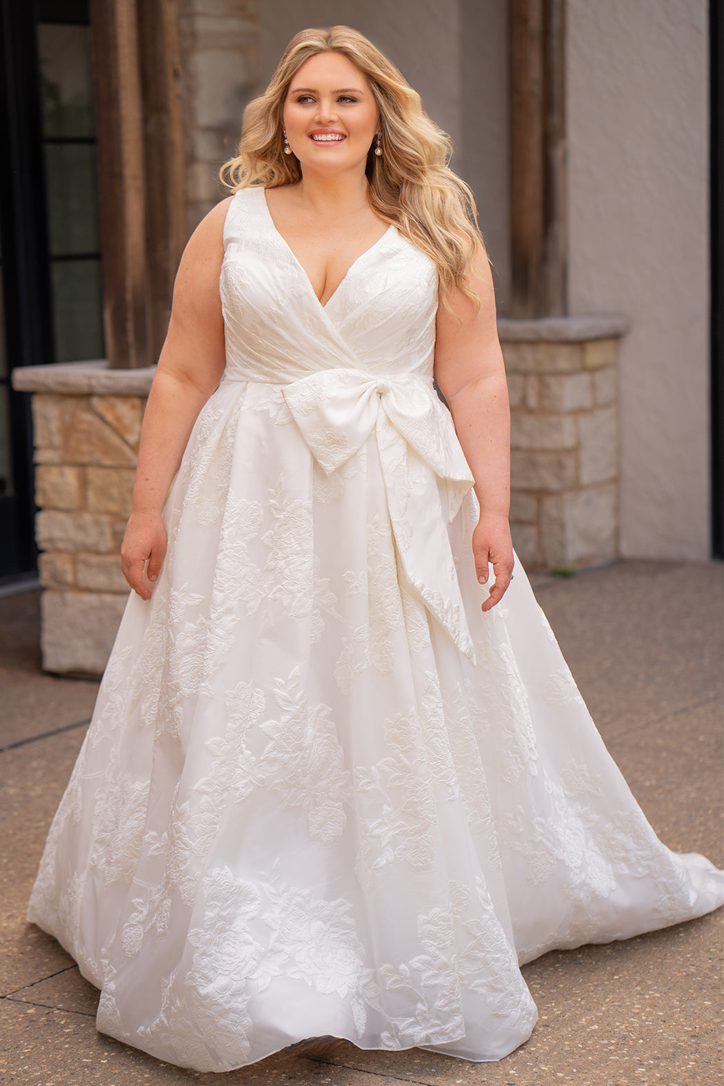 Michelle Bridal MB2625 shown in Ivory. 

Organza brocade A-line silhouette, Pleated faux surplice bodice for elegant shaping, Bra-friendly straps and sleeveless, detachable belt with oversized bow for two looks in one, Box-pleated A-line skirt with front slit for movement, Chapel-length train for timeless finish, Invisible center back zipper.