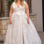 Michelle Bridal MB2625 shown in Ivory. 

Organza brocade A-line silhouette, Pleated faux surplice bodice for elegant shaping, Bra-friendly straps and sleeveless, detachable belt with oversized bow for two looks in one, Box-pleated A-line skirt with front slit for movement, Chapel-length train for timeless finish, Invisible center back zipper.