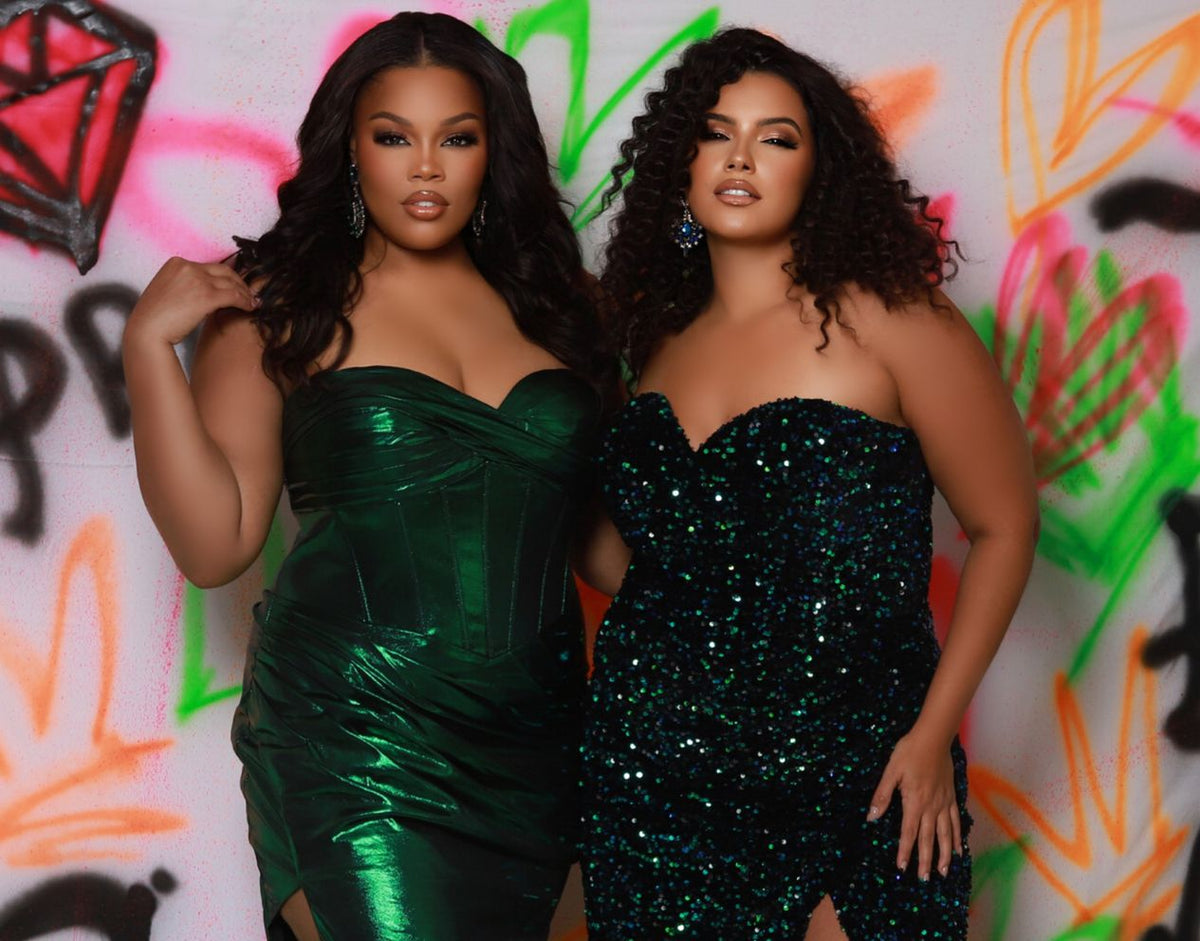 Two women in green strapless dresses standing against a colorful graffiti wall.