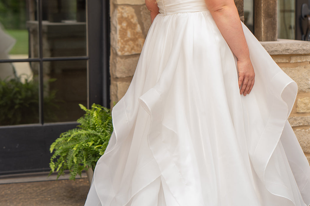 Woman in a white wedding dress standing outdoors near a stone wall.

Sydney's Closet style SC5359 pleated organza bridal gown with tiered ball gown skirt.