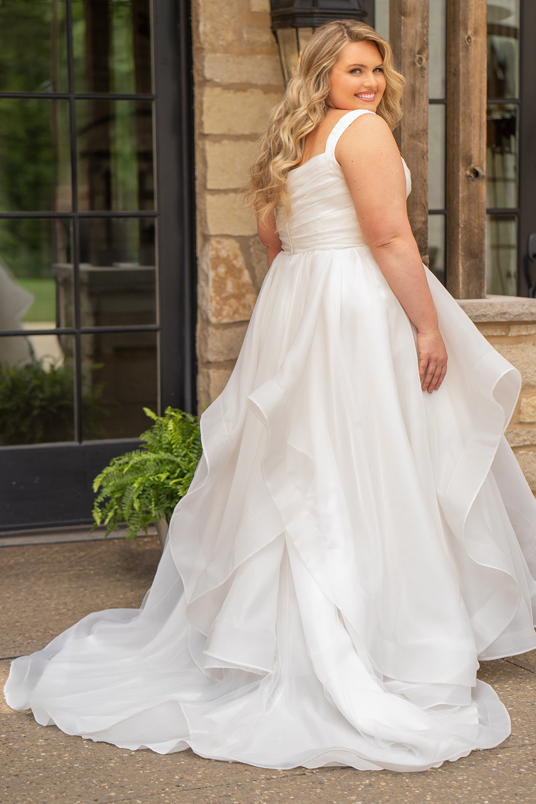 Woman in a white wedding dress standing outdoors near a stone wall.

Sydney's Closet style SC5359 pleated organza bridal gown with tiered ball gown skirt.