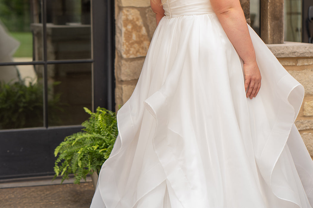 Woman in a white wedding dress standing outdoors near a stone wall.

Sydney's Closet style SC5359 pleated organza bridal gown with tiered ball gown skirt.