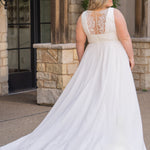 Woman wearing an ivory chiffon wedding dress standing outdoors.

Sydney's Closet style SC5360 in ivory/nude. Plus size light flowy chiffon bridal dress with pleated bodice and pleated waistband.  Illusion back covered in lace appliques with crystal buttons. Available in sizes 14-40. 