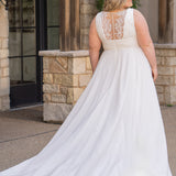 Woman wearing an ivory chiffon wedding dress standing outdoors.

Sydney's Closet style SC5360 in ivory/nude. Plus size light flowy chiffon bridal dress with pleated bodice and pleated waistband.  Illusion back covered in lace appliques with crystal buttons. Available in sizes 14-40. 