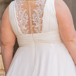 Woman wearing an ivory chiffon wedding dress standing outdoors.

Sydney's Closet style SC5360 in ivory/nude. Plus size light flowy chiffon bridal dress with pleated bodice and pleated waistband.  Illusion back covered in lace appliques with crystal buttons. Available in sizes 14-40. 