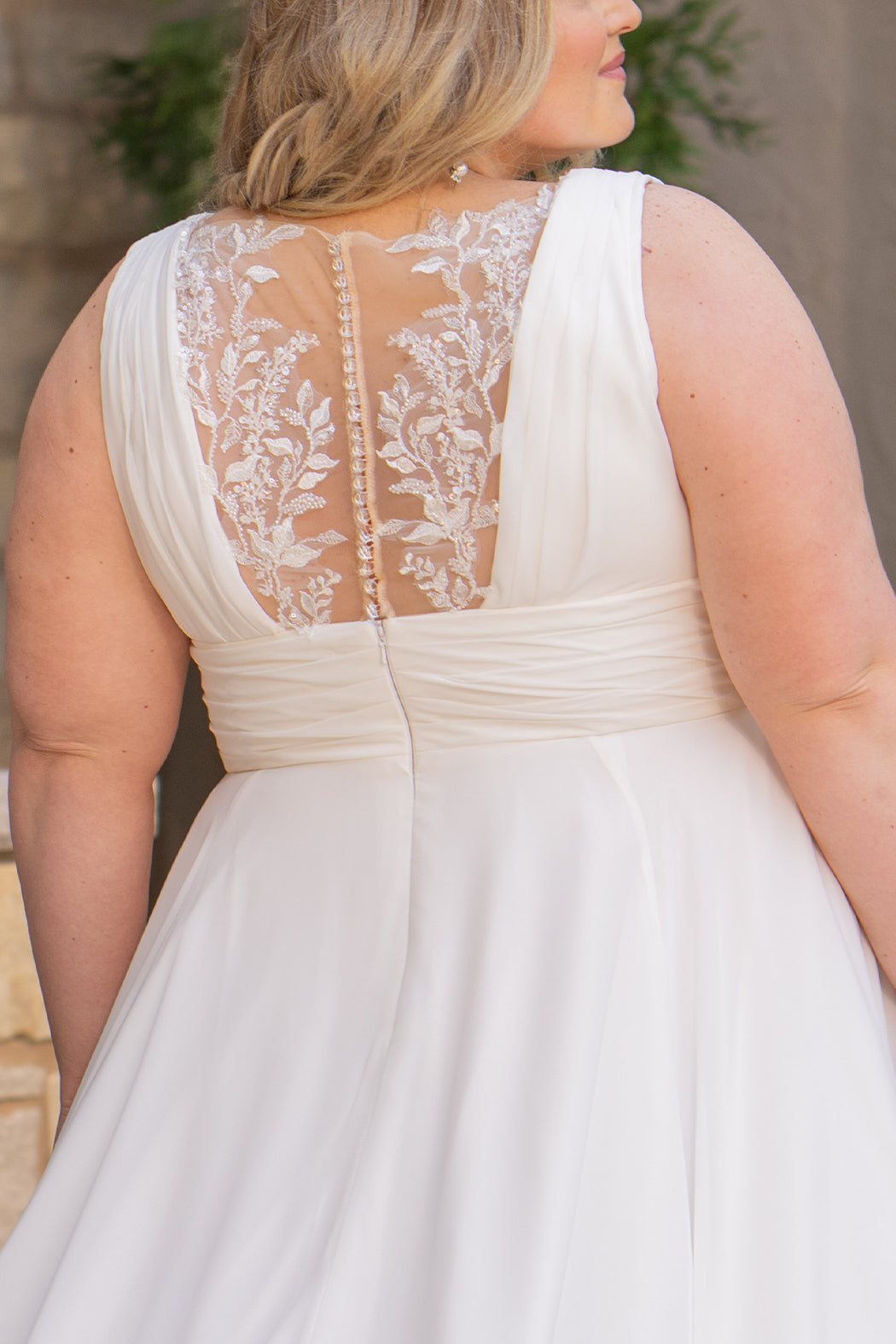 Woman wearing an ivory chiffon wedding dress standing outdoors.

Sydney's Closet style SC5360 in ivory/nude. Plus size light flowy chiffon bridal dress with pleated bodice and pleated waistband.  Illusion back covered in lace appliques with crystal buttons. Available in sizes 14-40. 