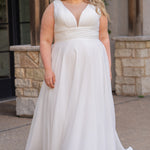 Woman wearing an ivory chiffon wedding dress standing outdoors.

Sydney's Closet style SC5360 in ivory/nude. Plus size light flowy chiffon bridal dress with pleated bodice and pleated waistband.  Illusion back covered in lace appliques with crystal buttons. Available in sizes 14-40. 