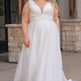 Woman wearing an ivory chiffon wedding dress standing outdoors.

Sydney's Closet style SC5360 in ivory/nude. Plus size light flowy chiffon bridal dress with pleated bodice and pleated waistband.  Illusion back covered in lace appliques with crystal buttons. Available in sizes 14-40. 