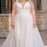 Woman wearing an ivory chiffon wedding dress standing outdoors.

Sydney's Closet style SC5360 in ivory/nude. Plus size light flowy chiffon bridal dress with pleated bodice and pleated waistband.  Illusion back covered in lace appliques with crystal buttons. Available in sizes 14-40. 